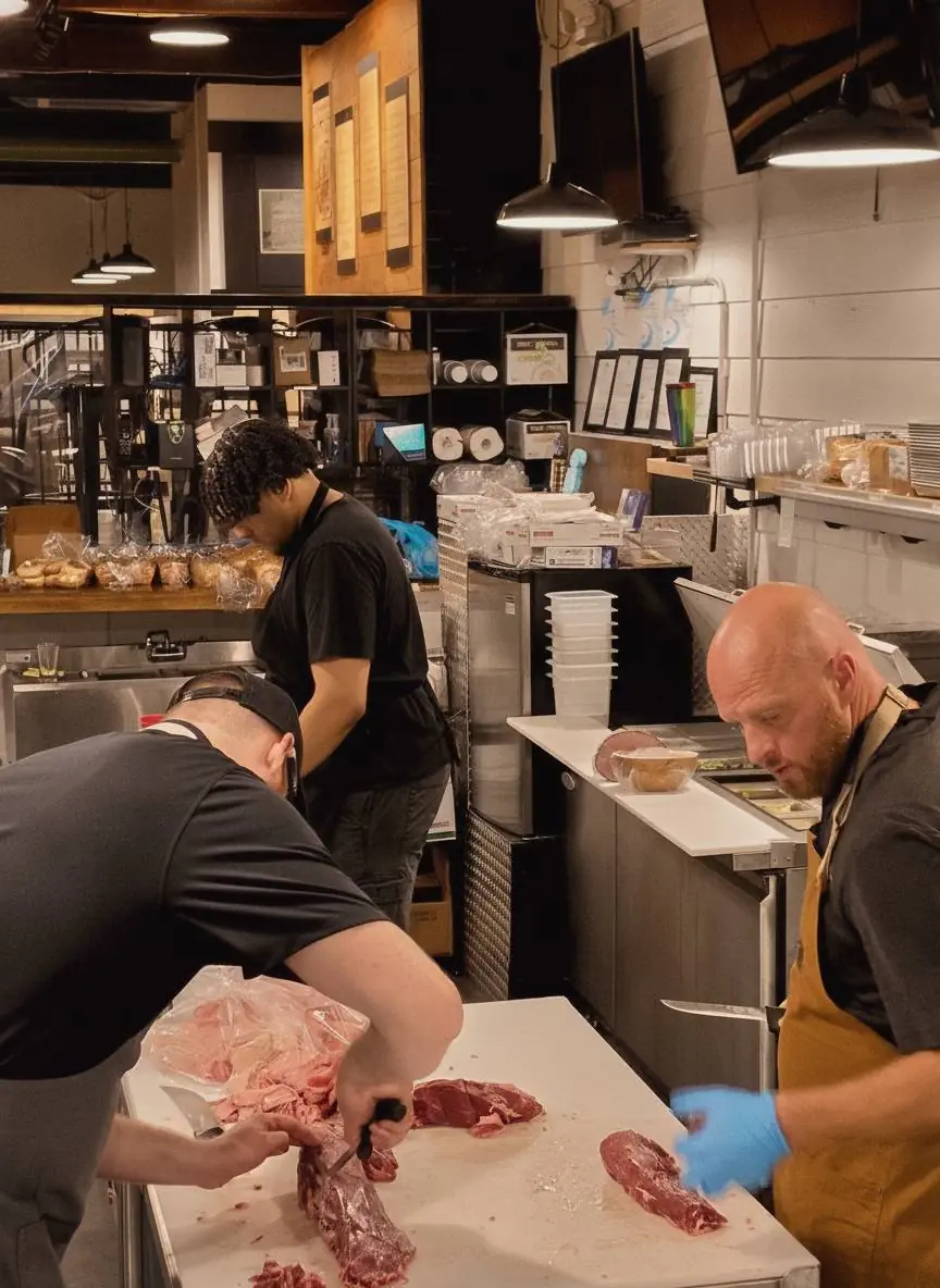 Three butchers breaking down whole cuts at the work table