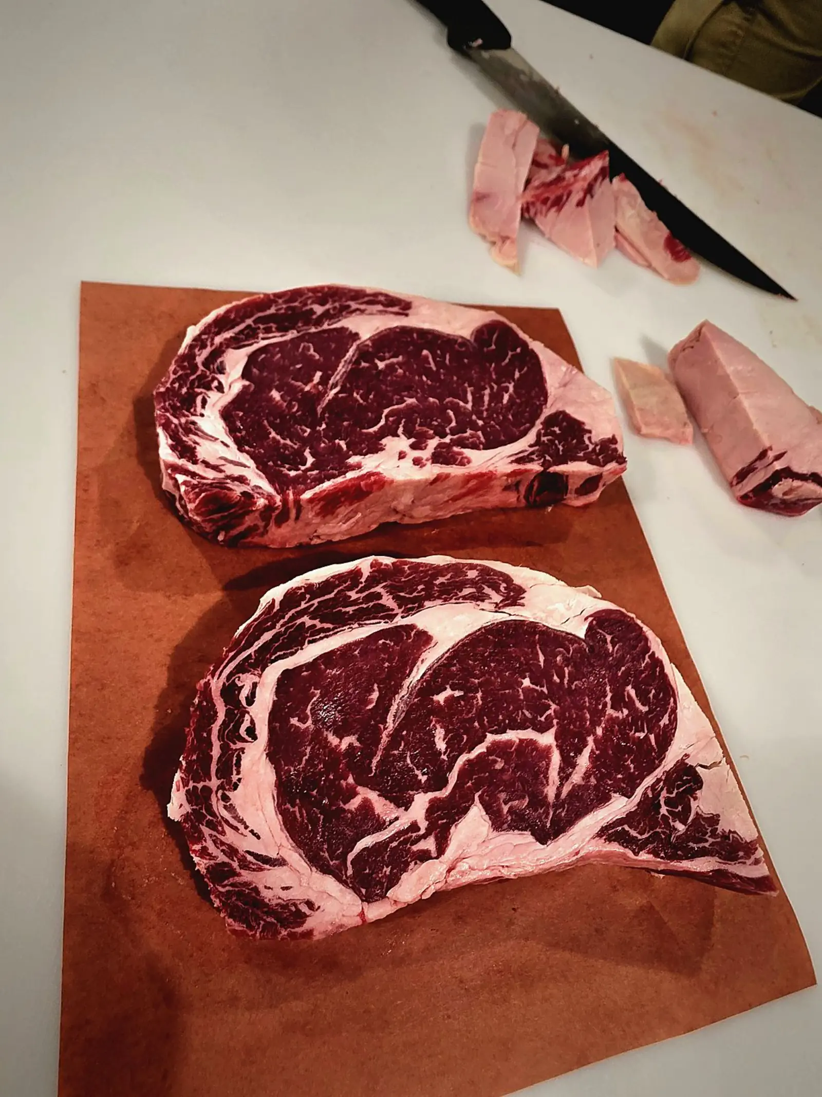 Two thick-cut ribeyes on butcher paper at the cutting table