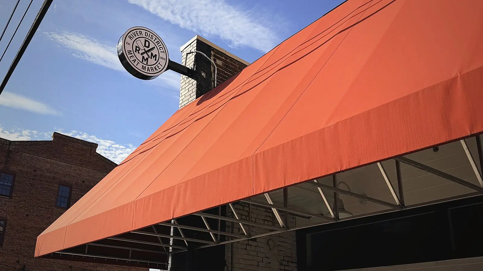 The round River District Meat Market sign over the red awning at 315 Lynn Street