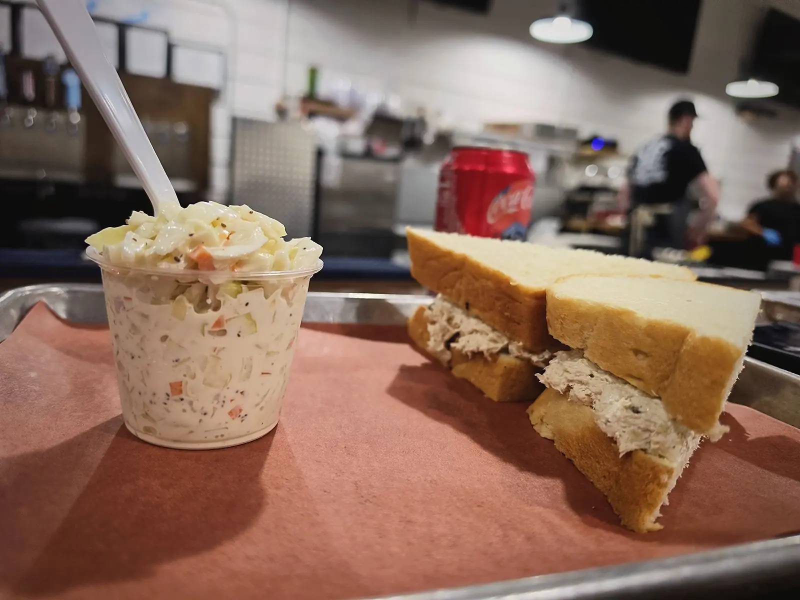 A chicken salad sandwich and cup of coleslaw on a lunch tray at the counter